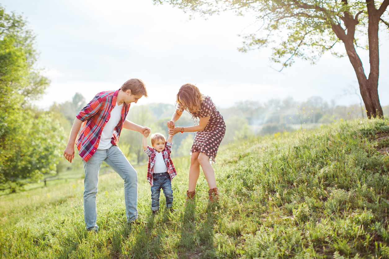 Parents holding a child's hands on a hillside